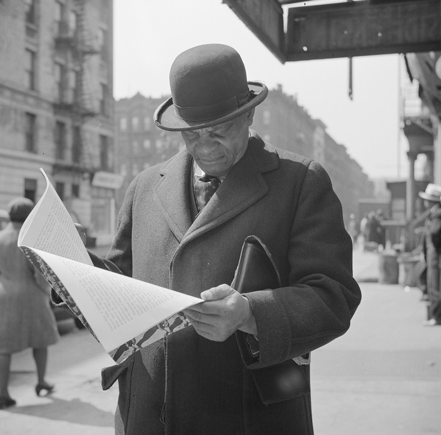 New York, New York. A. Marcus Garveyite reading the OWI (Office of War Information) publication Negroes and the War, April 1943. Library of Congress Prints and Photographs Division, Washington, D.C. 20540, USA. OWI was the Executive Branch agency under the control of the White House. Its Overseas Division produced World War II shortwave radio broadcasts, which were later named the Voice of America (VOA).